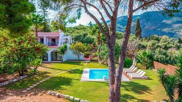 A house with a swimming pool, surrounded by a well-maintained lawn and trees.