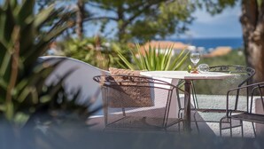 Een buiten eethoek met een tafel en stoelen, een glas wijn en uitzicht op zee.