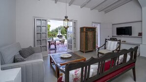 Een ruime woonkamer met een bank, een eettafel en stoelen. Er is een televisie aan de muur bevestigd en een kast met decoratieve objecten.