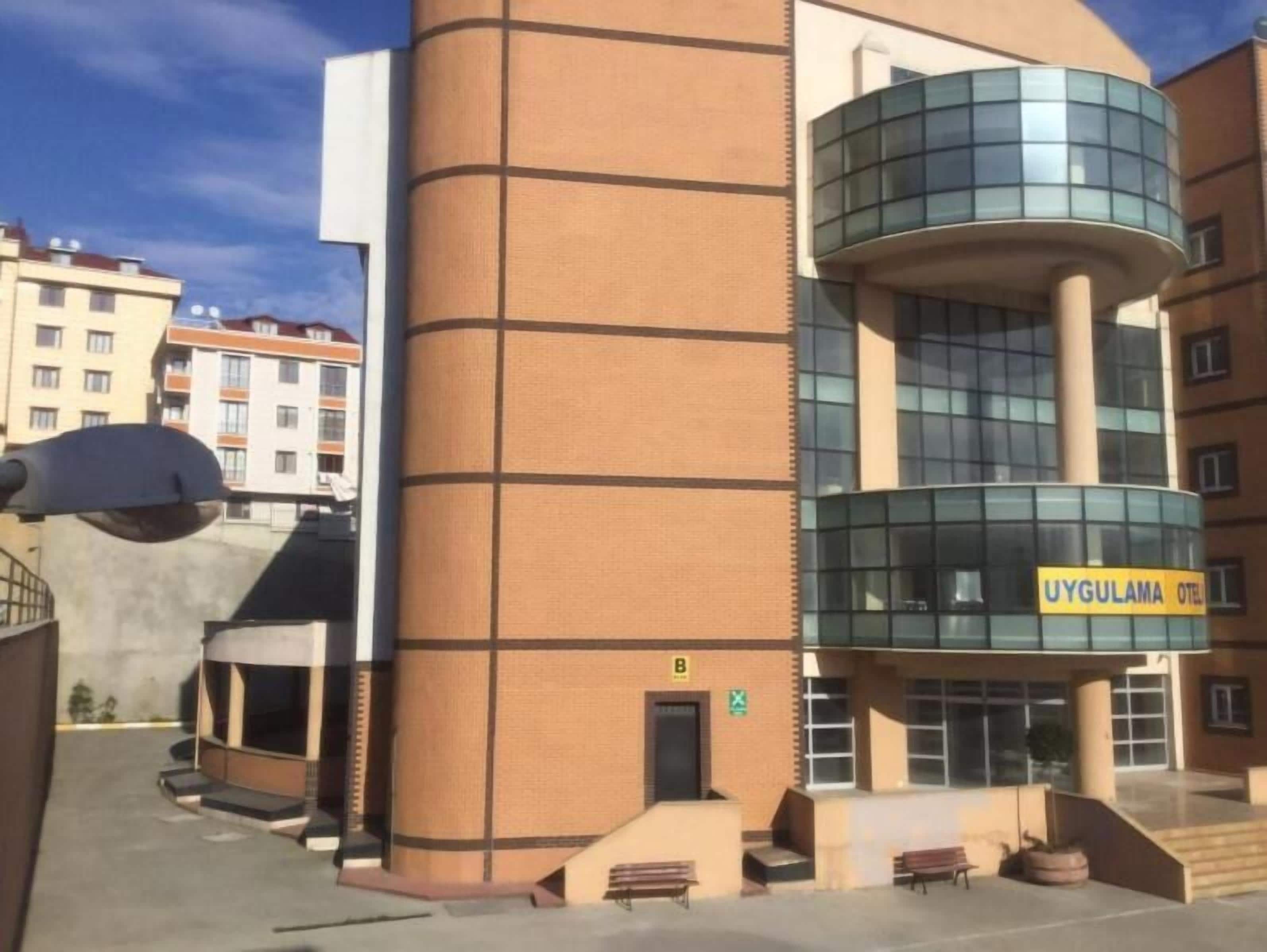 A modern building with a curved glass facade and a sign reading "UYGULAMA HOTEL".