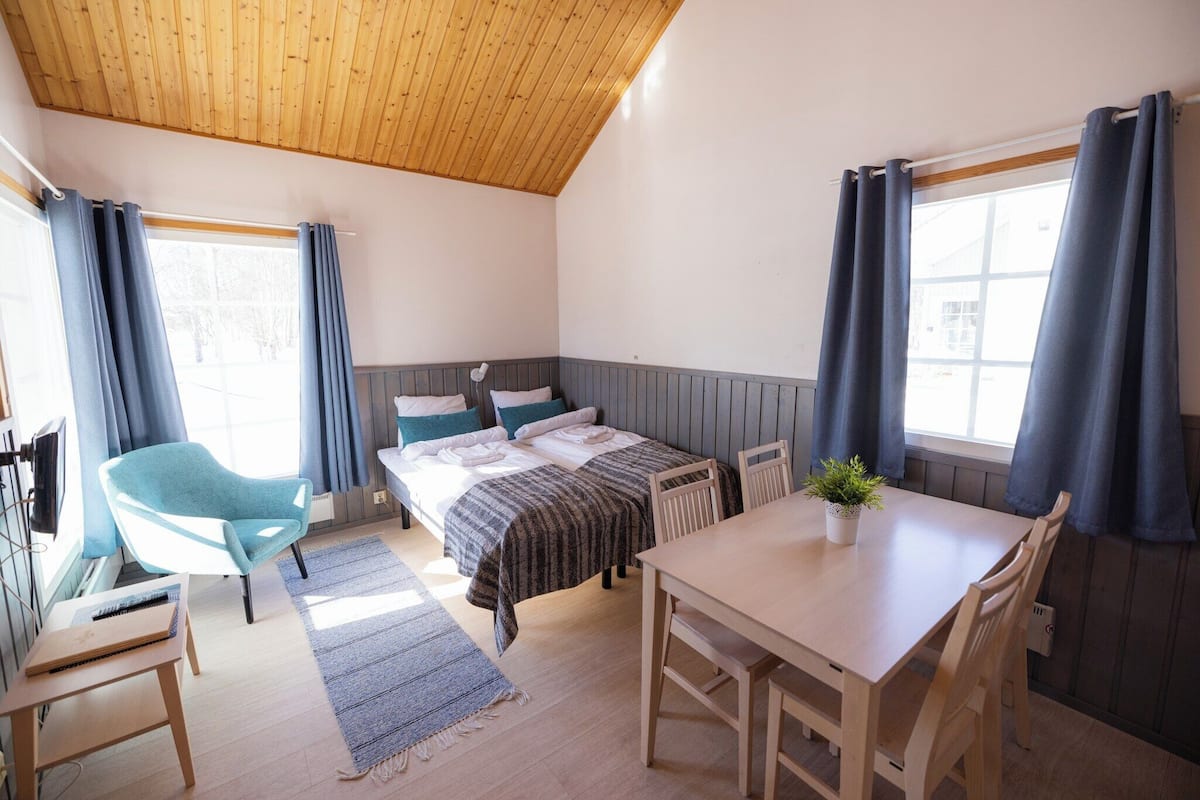 Una habitación con cama, silla, mesa y ventana.