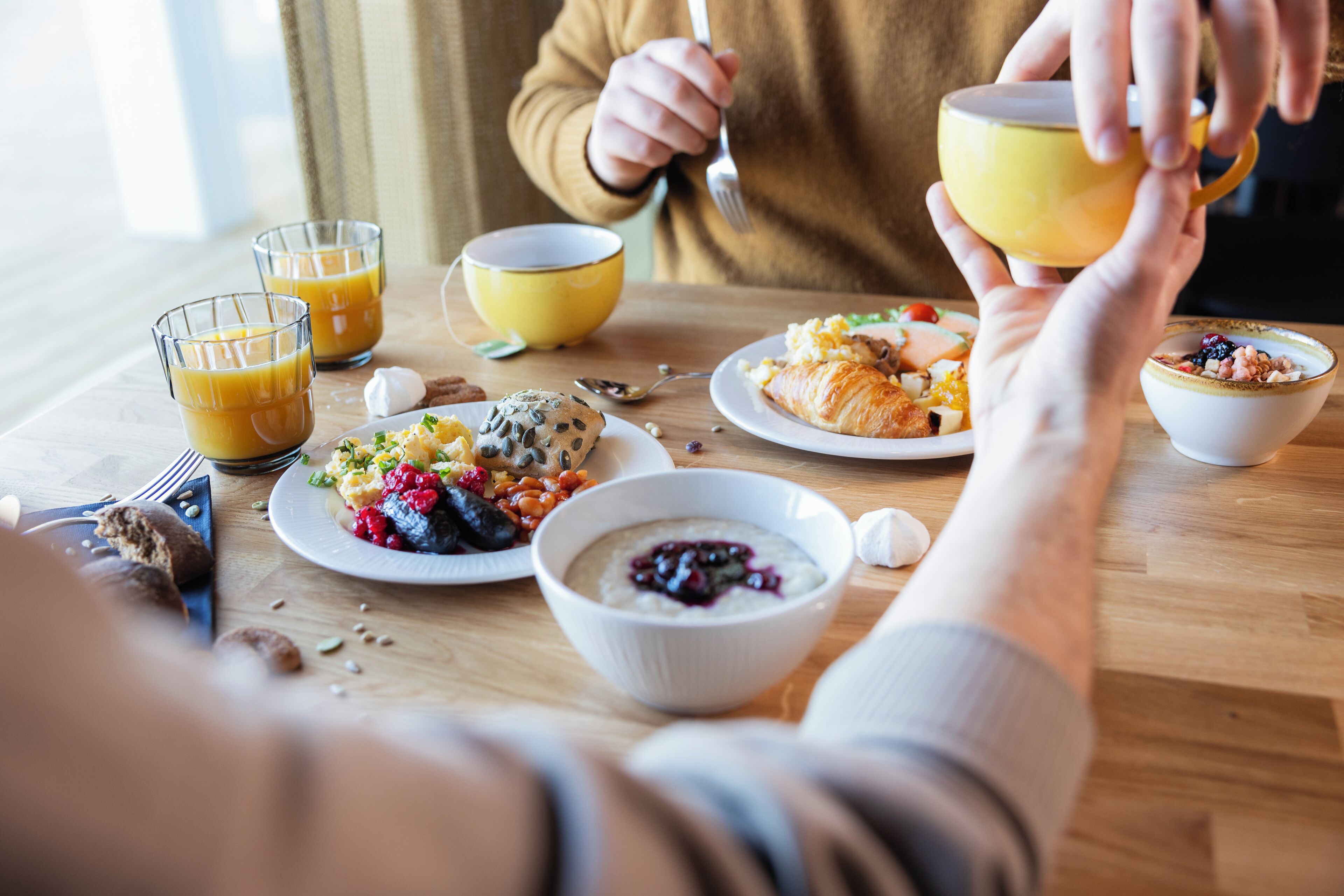 A breakfast setting with various dishes, including eggs, pastries, and a croissant, on a wooden table.