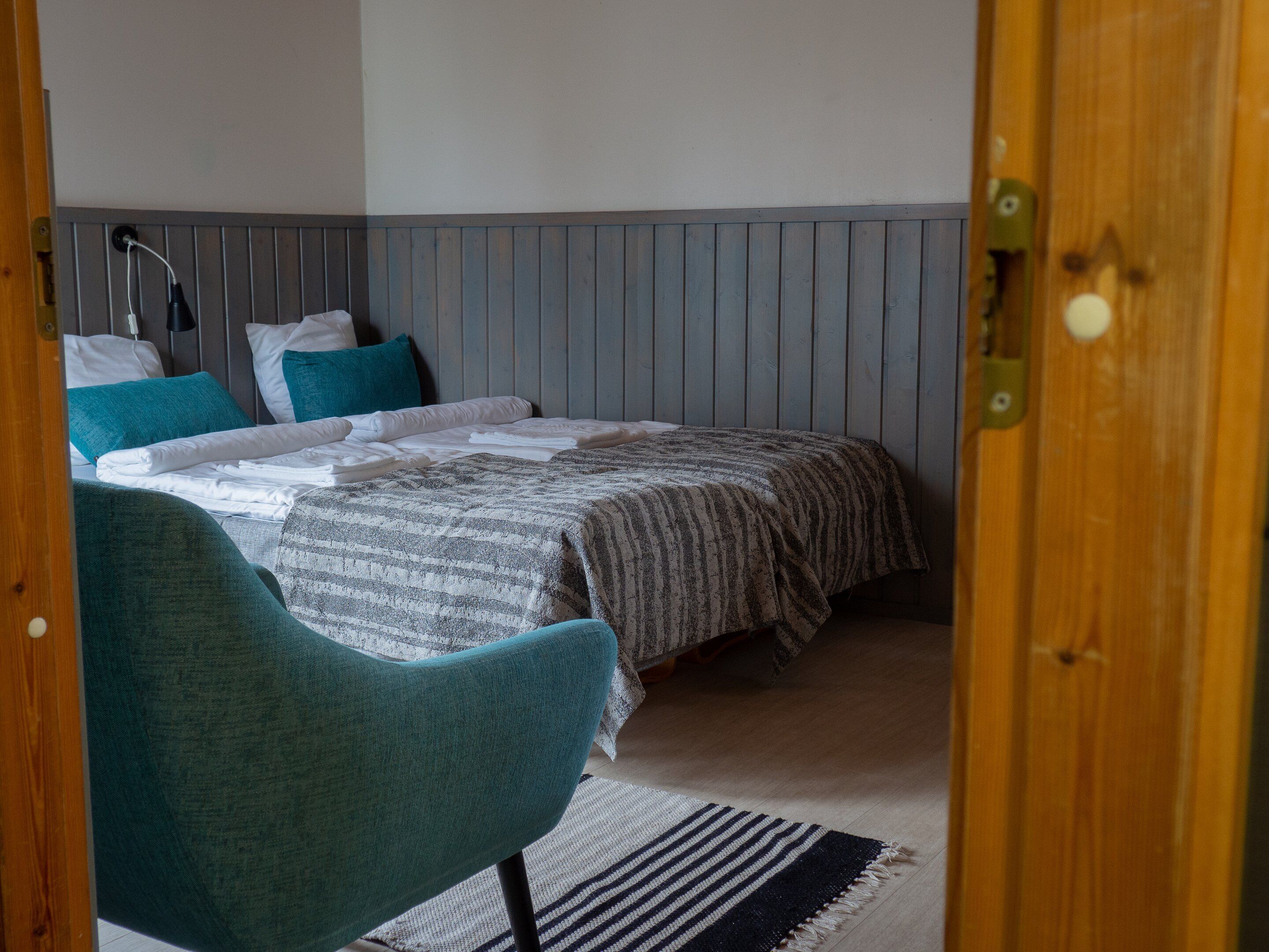 Um quarto com uma cama, uma cadeira, uma mesa de cabeceira e uma porta de madeira.