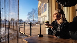 Eine Person sitzt an einem Tisch mit Blick auf ein Gebäude und einen Zaun.