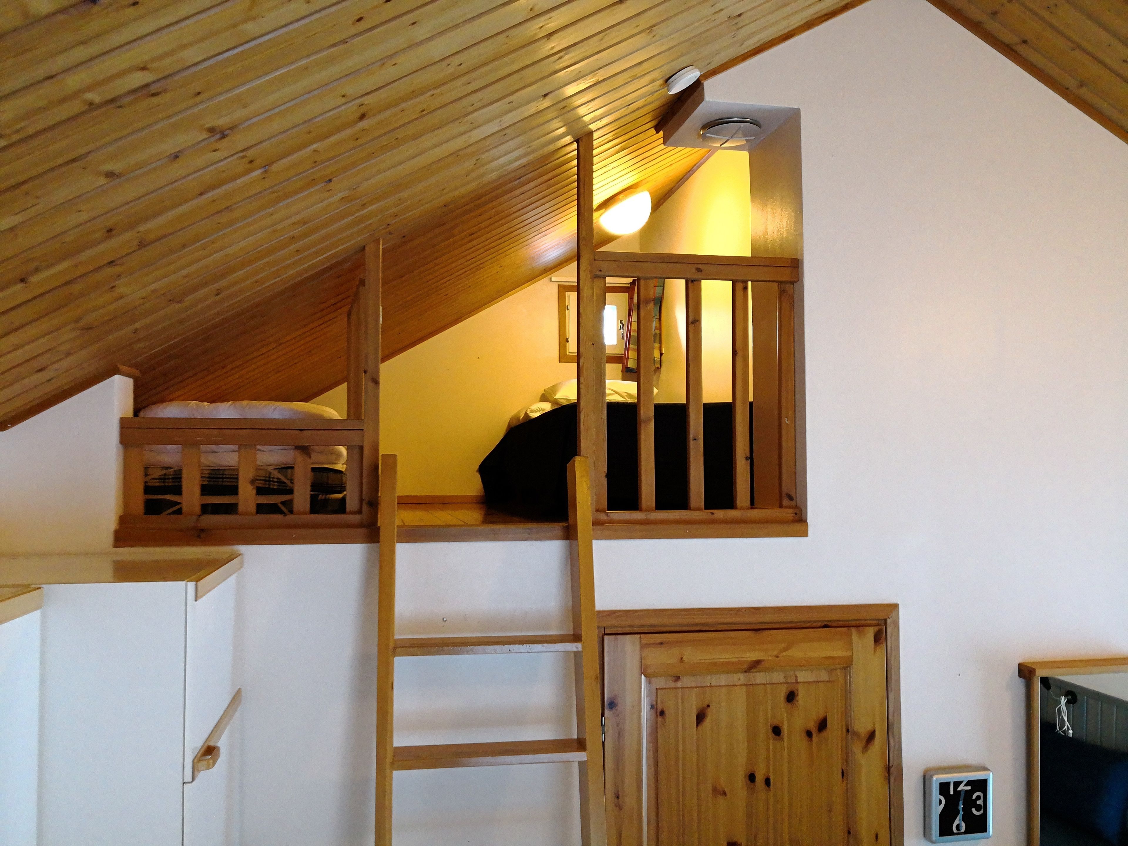Quarto estilo loft com beliche, escada e uma pequena janela.