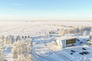 Een besneeuwd landschap met een modern gebouw, een parkeerplaats en sneeuwzware bomen.