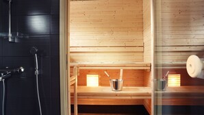 Eine Sauna mit Holzbänken, einer Glastür und einem Metall-Eimer mit einem Löffel.