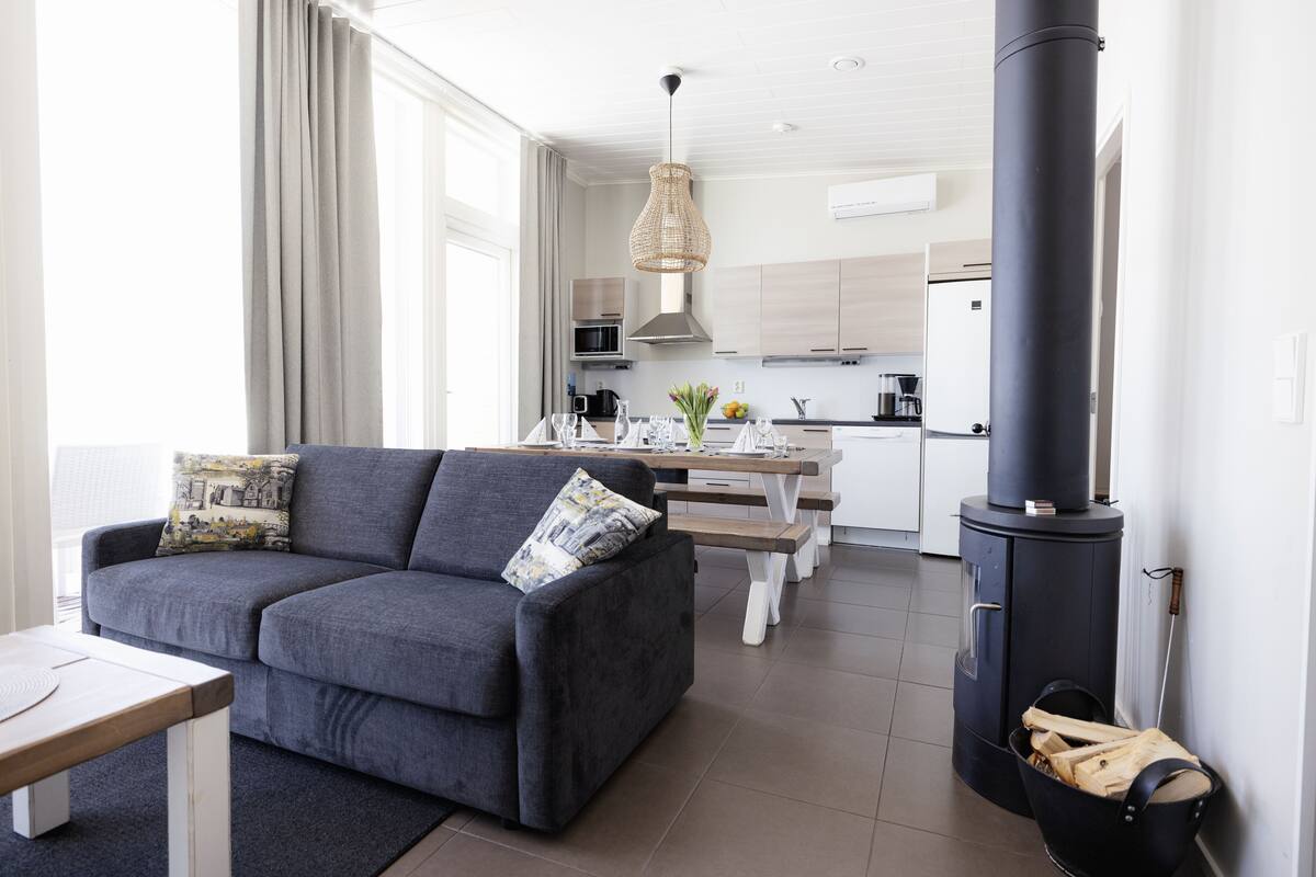 Una sala de estar moderna con un sofá gris, una mesa de centro de madera y un estufa de leña negra.