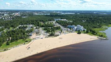 An aerial view of a coastal area with a sandy beach, a marina, and a mix of residential and commercial buildings.