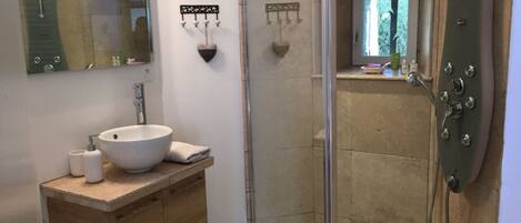 A bathroom with a wooden vanity, a white sink, a glass shower enclosure, and a window with a view of greenery.