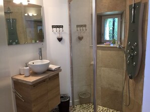 A bathroom with a wooden vanity, a white sink, a glass shower enclosure, and a window with a view of greenery.