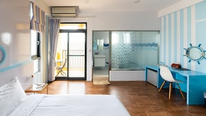 Habitación de hotel con cama, escritorio, silla, ventana con cortinas y vista al balcón.