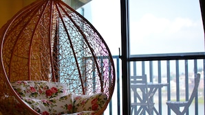 Una silla colgante de mimbre con cojines estampados, ubicada cerca de un balcón con barandilla de madera.