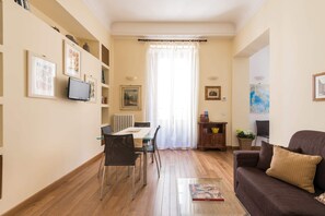 Un salon avec un canapé marron, une table basse, une table à manger avec des chaises et un téléviseur fixé au mur.