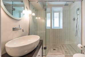 Une salle de bain moderne avec un grand lavabo ovale, une douche en verre et une fenêtre bien visible.