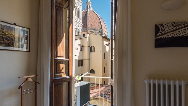 A narrow corridor with a view of a historic building with a dome, a radiator, and a framed picture on the wall. - Charming 2bed Apt Overlooking Duomo (Florence)