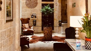A cozy room with a stone wall, a chandelier, a fireplace, a leather armchair, a wooden coffee table, and a potted plant. - Casa Birmula (Cospicua)