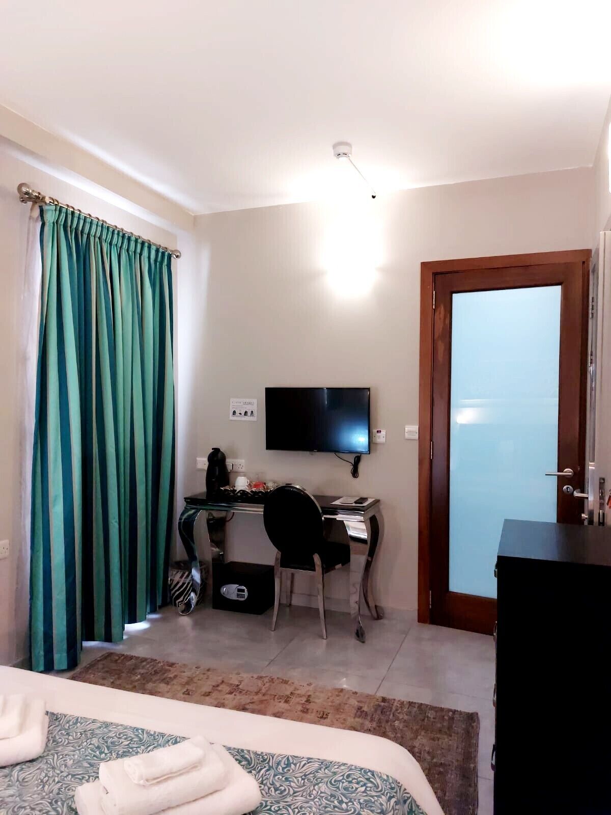 A hotel room with a bed, a desk with a computer, a television, and a door with frosted glass.