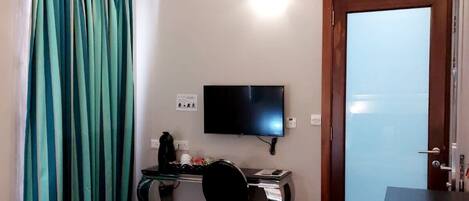 Hotellihuone, jossa on sänky, työpöytä tietokoneella, televisio ja ovi, jossa on himmeä lasi.