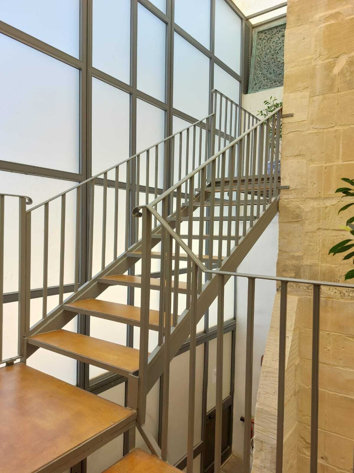 Una escalera con barandillas de metal y escalones de madera que lleva a un piso superior.