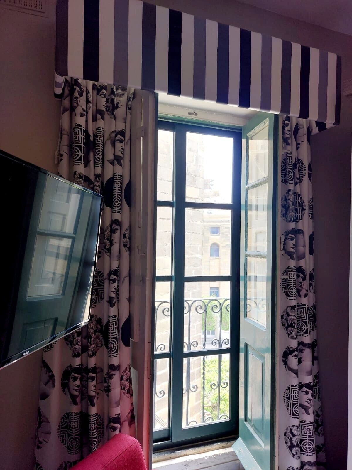 A room with a large window, striped curtains, and a flat-screen TV.