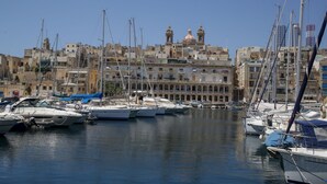 A marina with boats docked, a clear sky, and buildings in the background. - Casa Birmula (Cospicua)