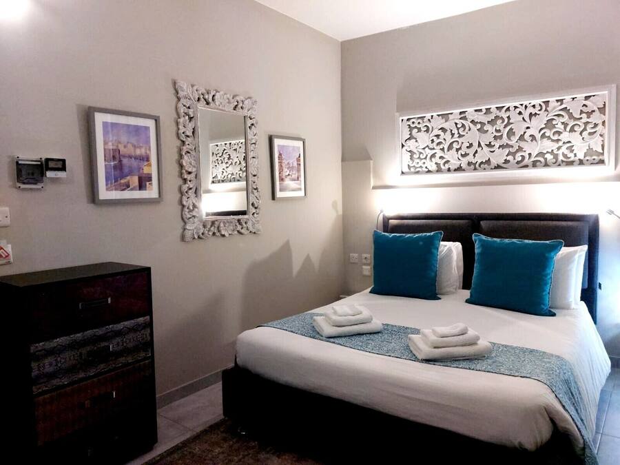 Un dormitorio con cama, dos mesitas de noche, cómoda y decoración mural.
