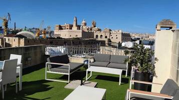 Una terraza en la azotea con mobiliario exterior, vistas panorámicas de la ciudad y una grúa de construcción al fondo.