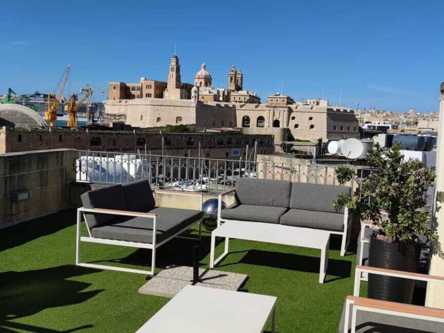 Una terraza en la azotea con mobiliario exterior, vistas panorámicas de la ciudad y una grúa de construcción al fondo.