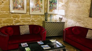 Una habitación con pared de piedra, dos sofás rojos, una mesa de centro de vidrio con revistas y tres obras de arte enmarcadas en la pared.