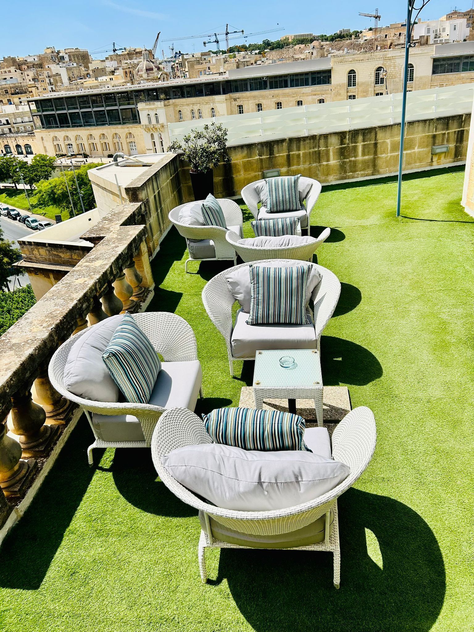 A rooftop terrace with wicker furniture, a small table, and a view of the cityscape.