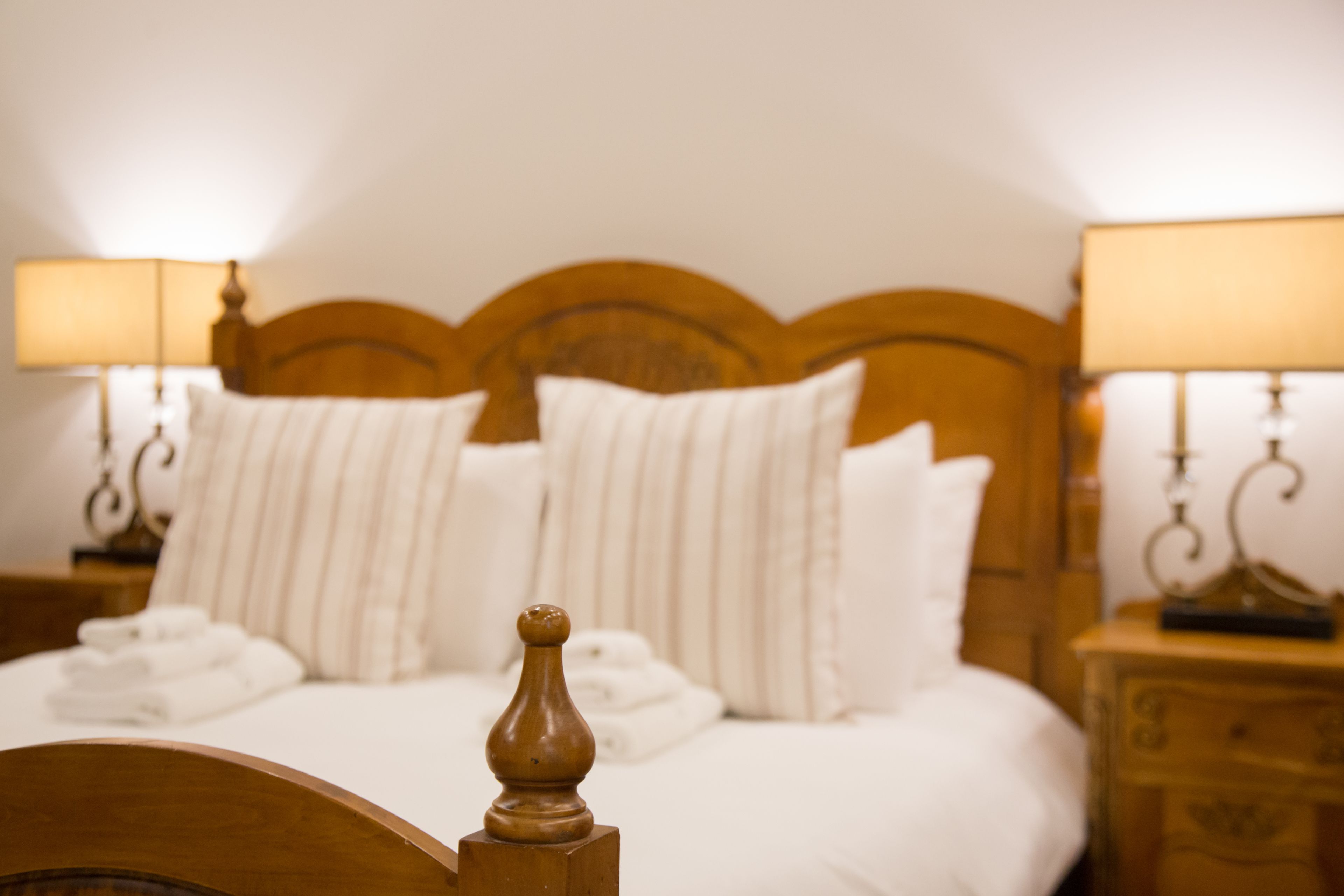 A neatly made bed with white linens and striped pillows, flanked by two bedside tables with lamps.