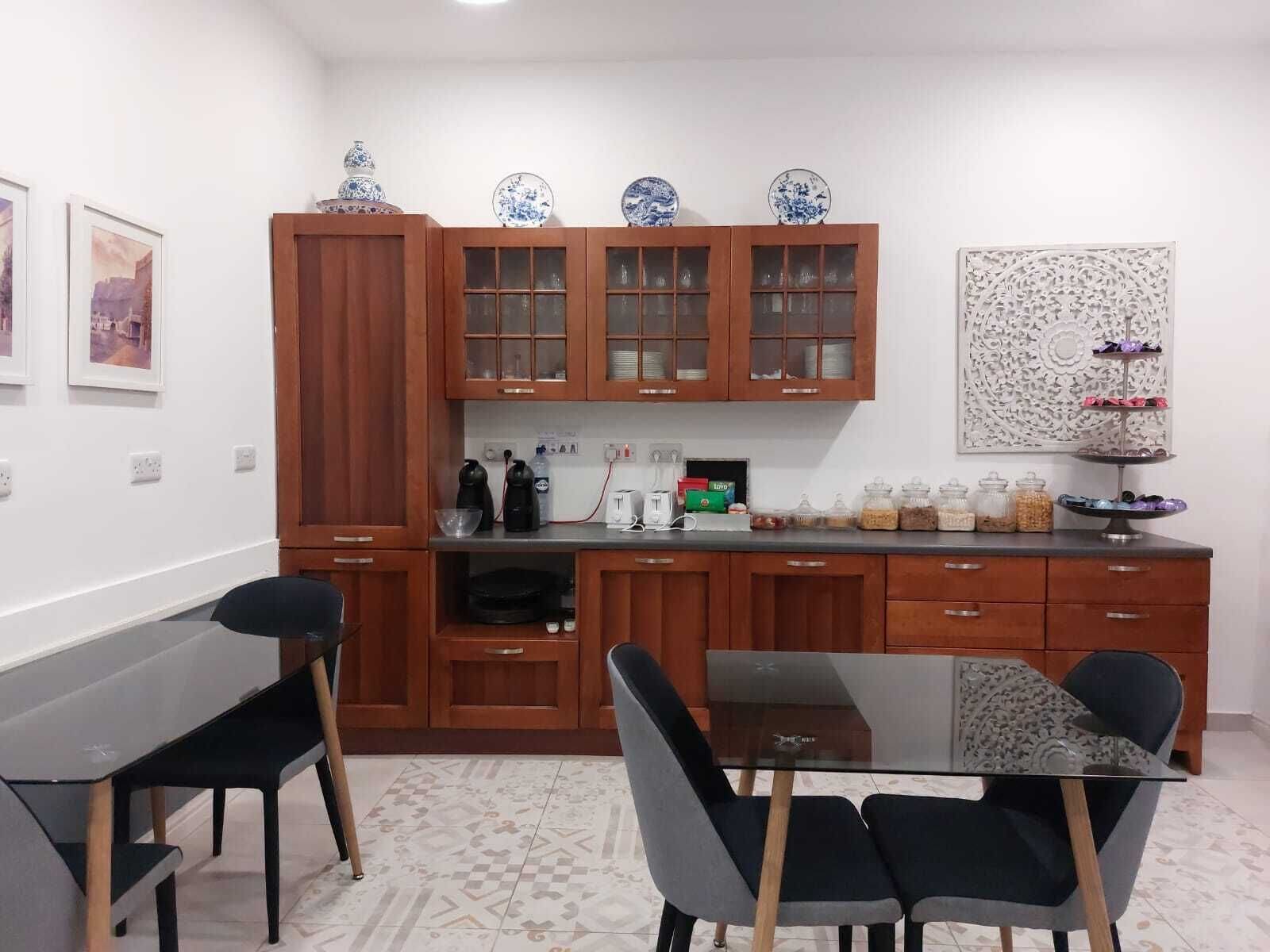 Una cocina compacta con armarios de madera, una mesa de comedor con cubierta de vidrio y sillas modernas.