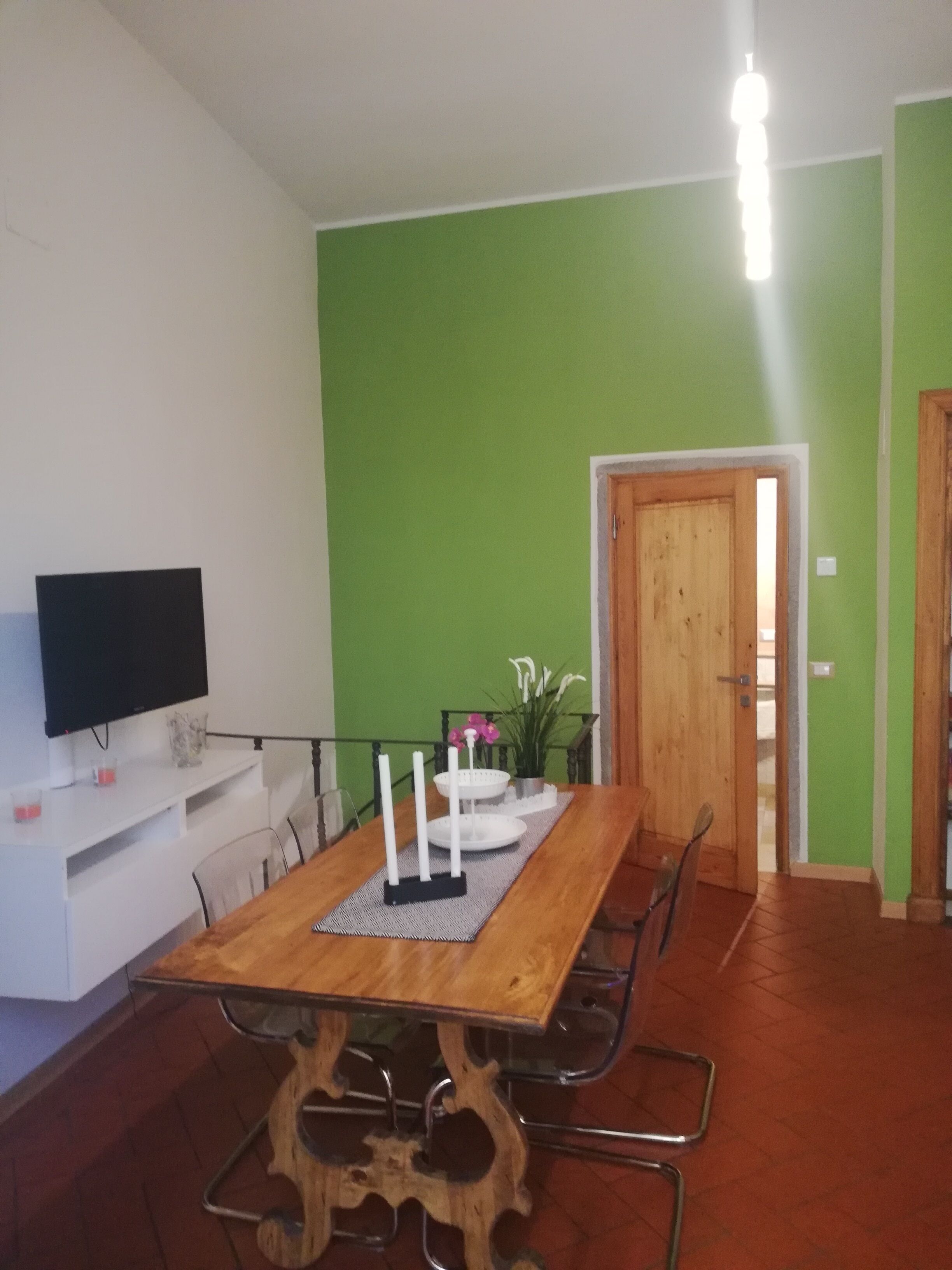 Ein Essbereich mit einem Holztisch, Stühlen, einem Fernseher auf einem weißen Schrank und einer grünen Wand.