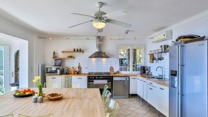 Eine moderne Küche mit Essbereich, ausgestattet mit einer zentralen Kochinsel, Edelstahlgeräten und einem Deckenventilator.