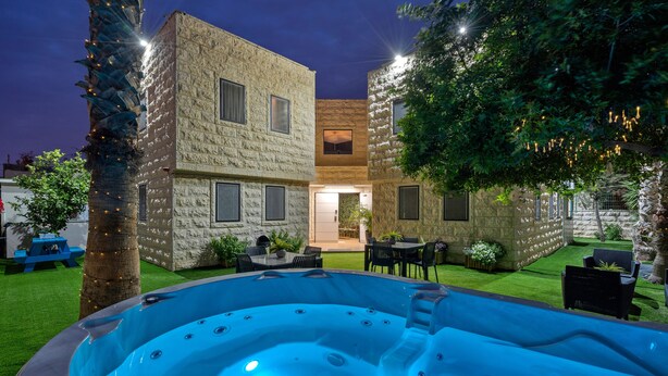 Een modern buitenzwembad met een jacuzzi, omringd door stenen gebouwen en groen.