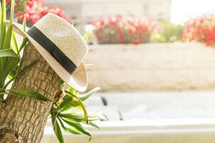 Un sombrero apoyado en el tronco de un árbol, con un fondo desenfocado de flores y una fuente.