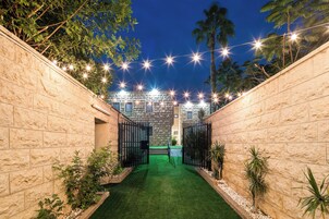 Un patio con muro de piedra, césped artificial verde y palmeras.