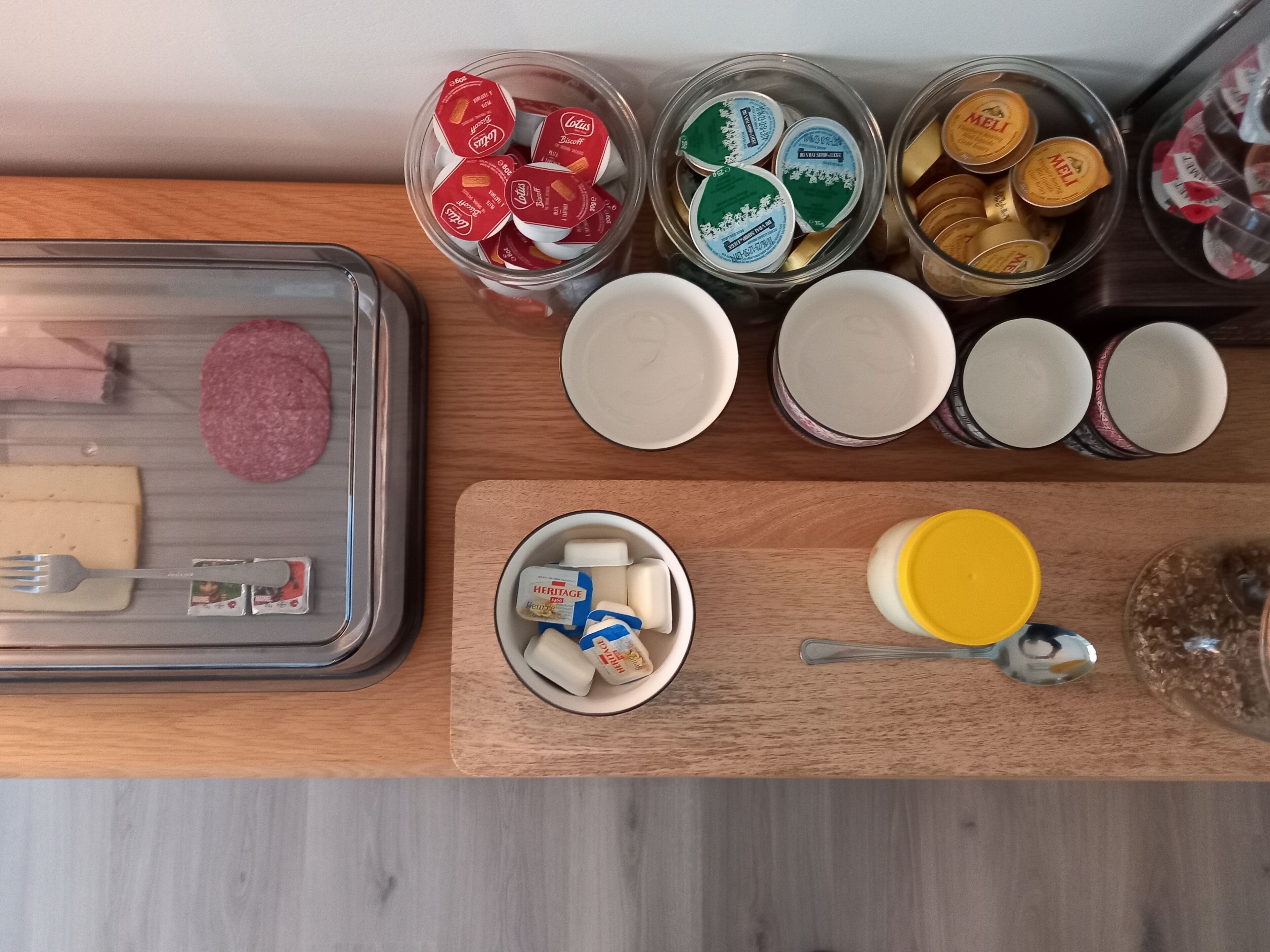 A kitchen counter with various food items and containers, including jars of honey, a tray with cheese and meat, and a bowl with butter and a spoon.
