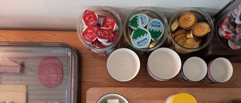 A kitchen counter with various food items and containers, including jars of honey, a tray with cheese and meat, and a bowl with butter and a spoon.