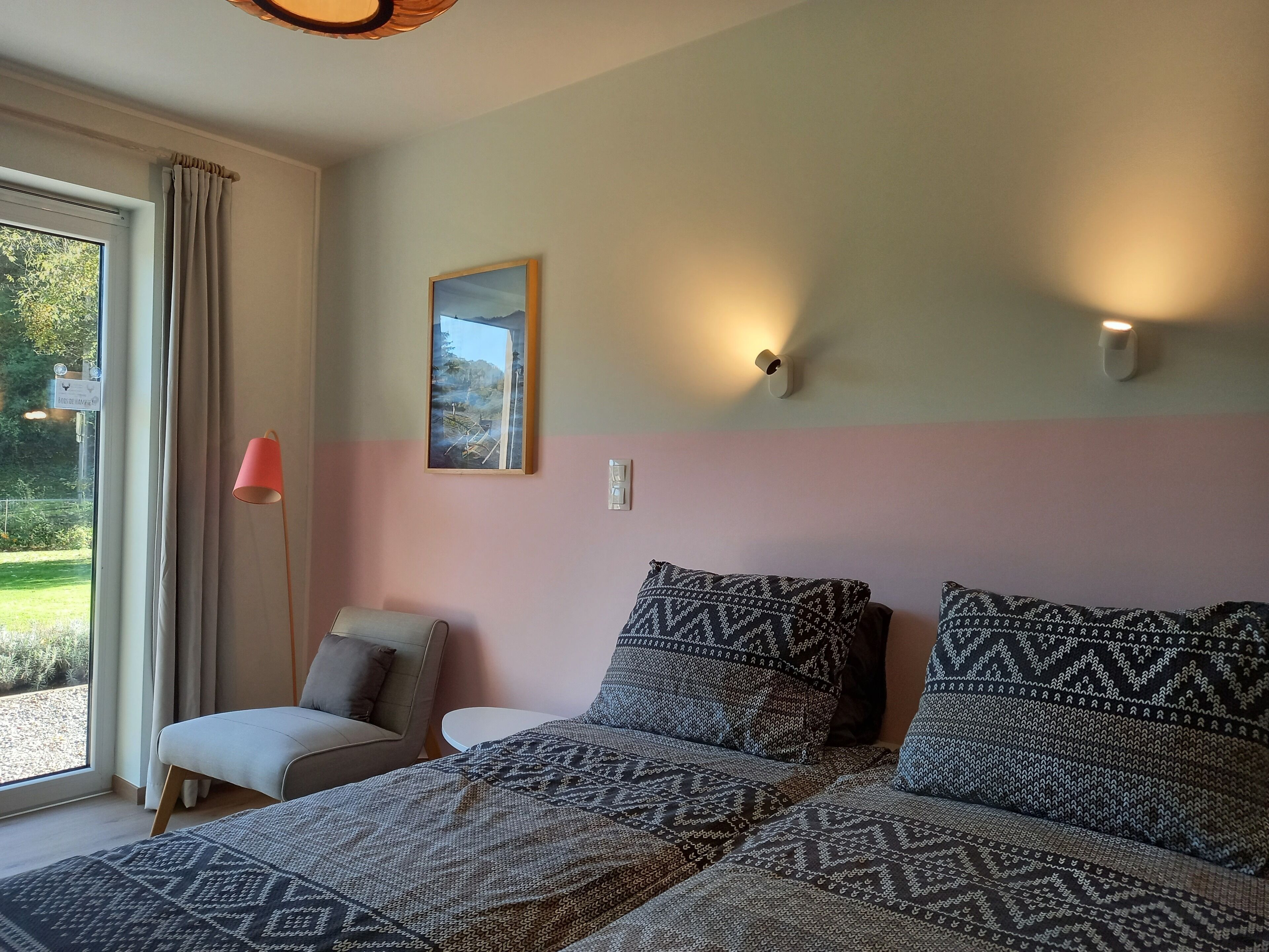 Un dormitorio con una cama, una silla, una mesa, un cuadro y una ventana con cortinas.
