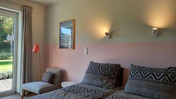 Un dormitorio con una cama, una silla, una mesa, un cuadro y una ventana con cortinas.