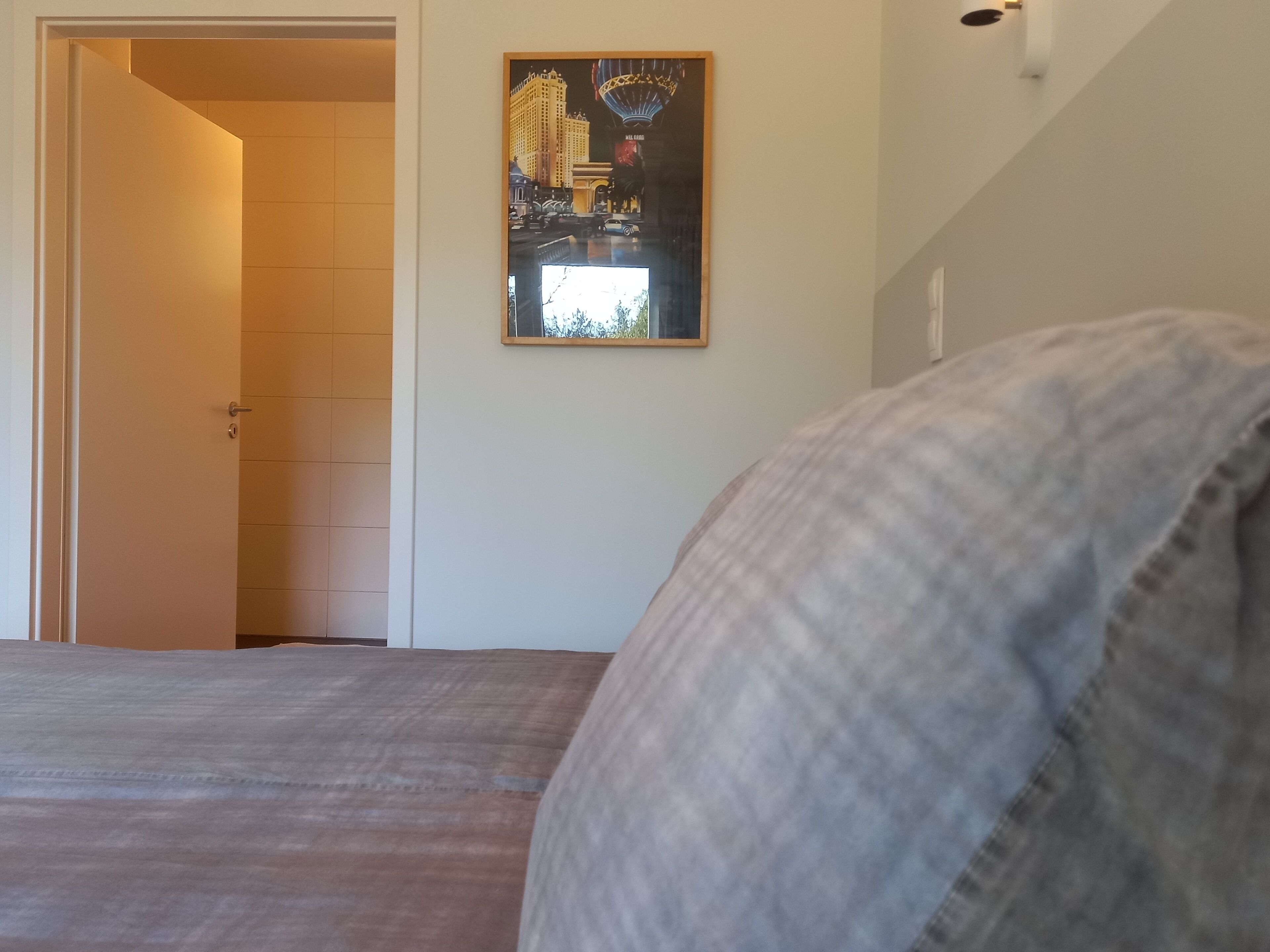 A bedroom with a bed, a door leading to another room, and a framed picture on the wall.