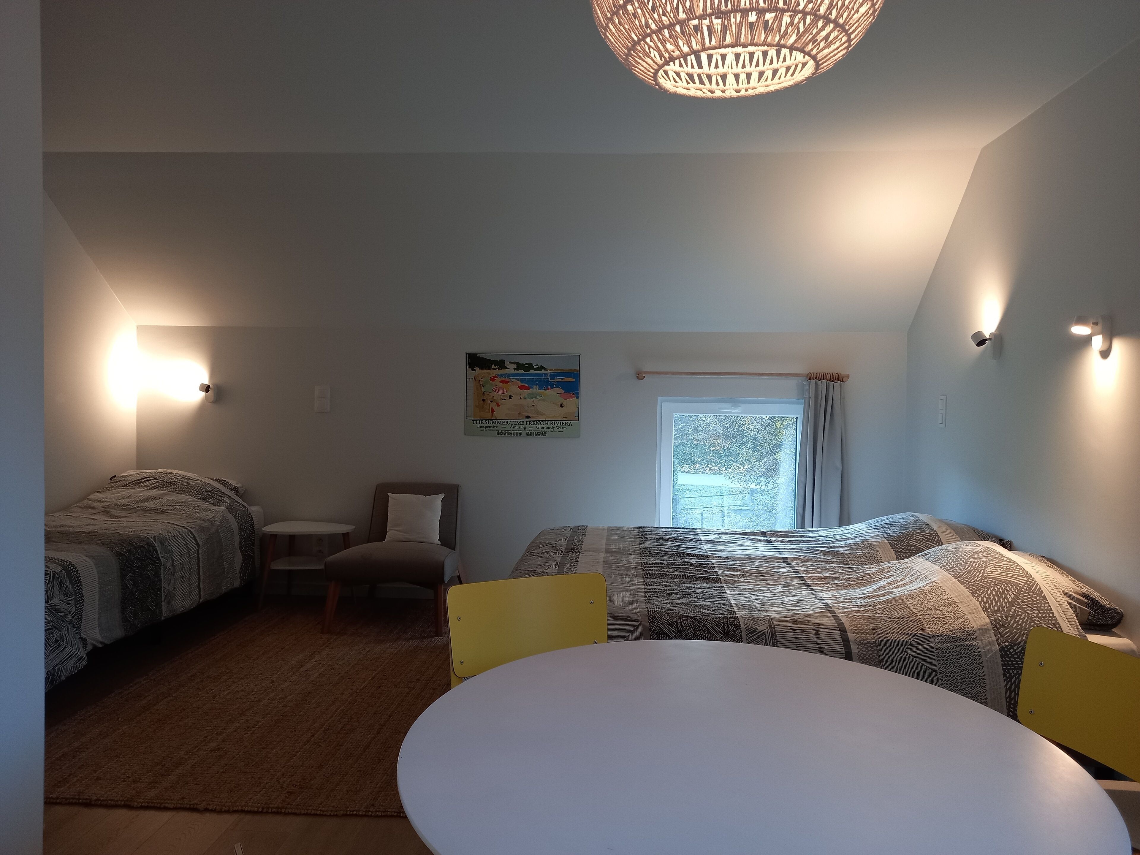 Una habitació amb un llit, dues taules de nit, una cadira, una taula i una finestra amb cortines.
