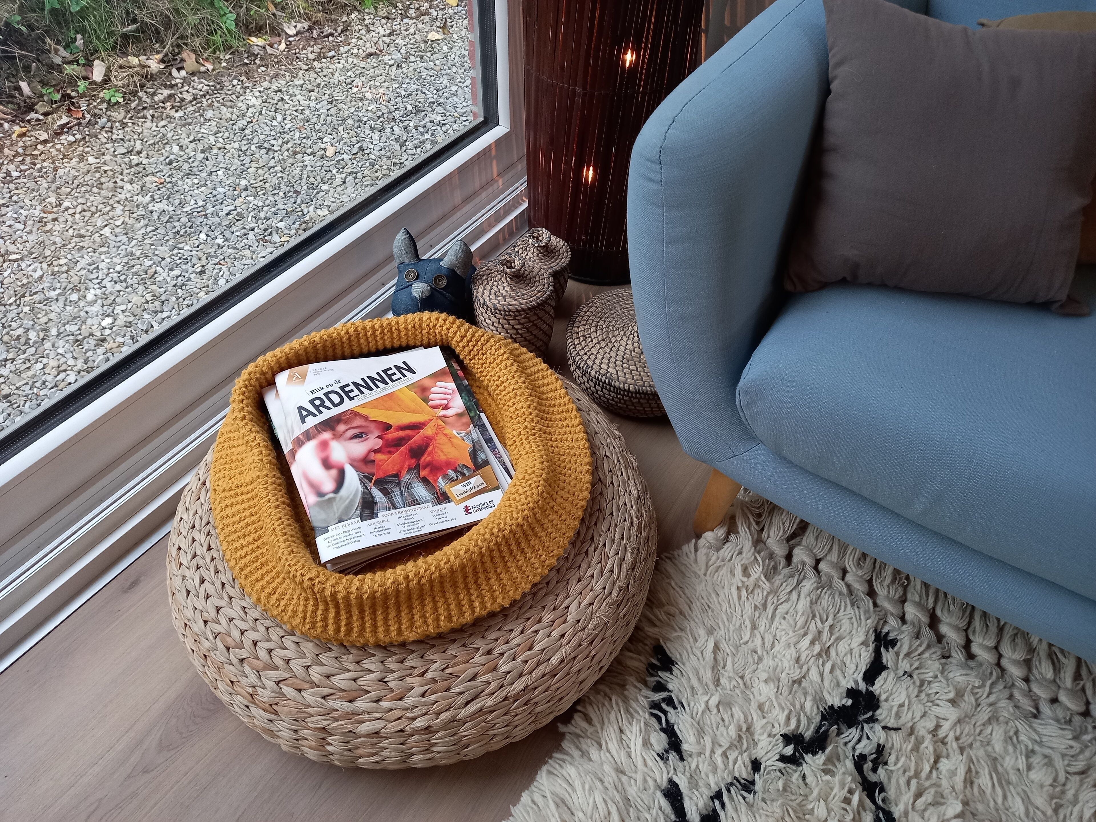 A cozy room with a woven basket containing a magazine, a blue sofa, and a woven rug.