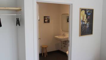 Een badkamer met een witte wastafel, een spiegel en een houten krukje. Twee ingelijste foto's hangen aan de muur.