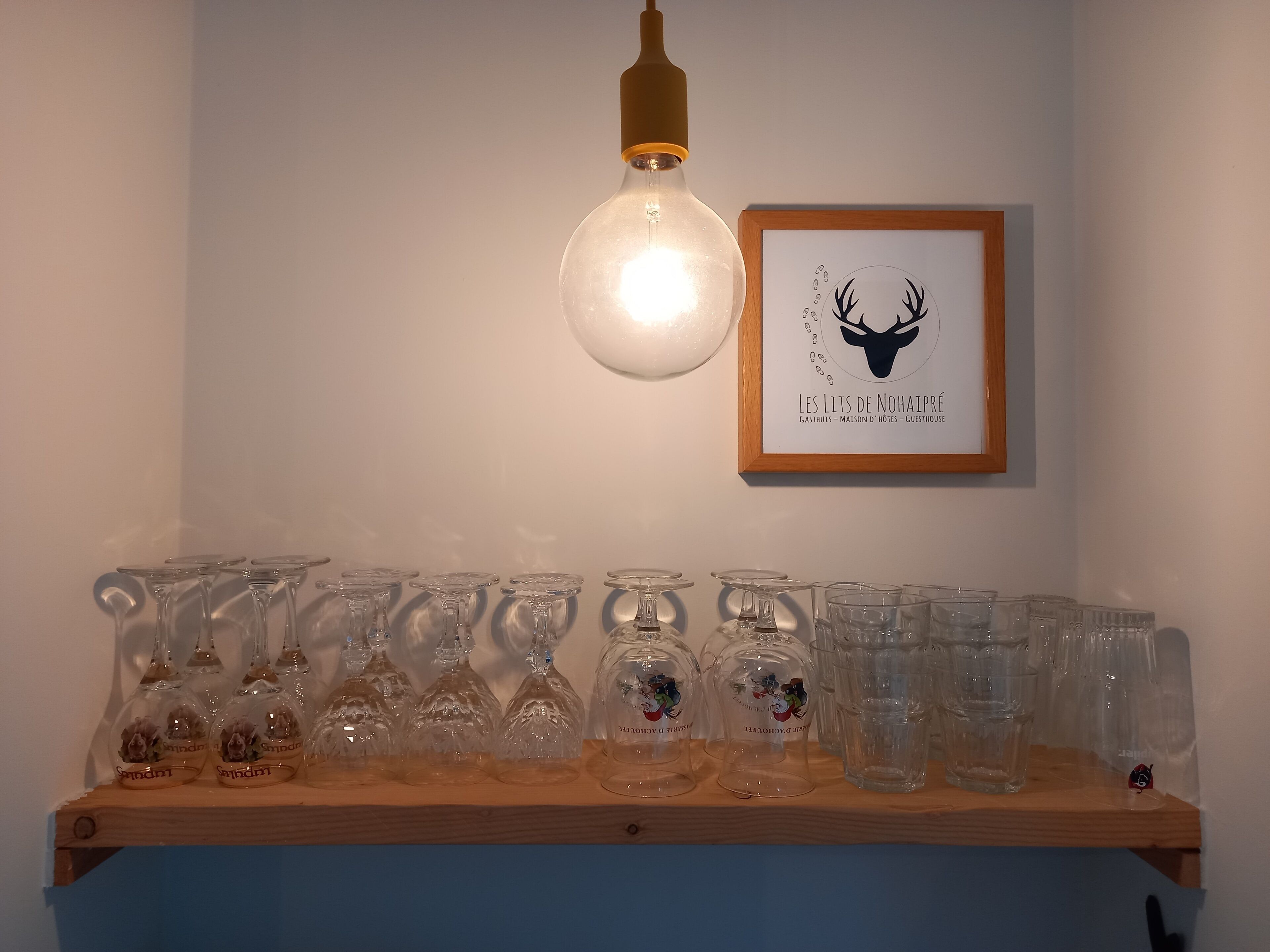 A shelf with various glassware, a framed picture of a deer head, and a hanging light bulb.