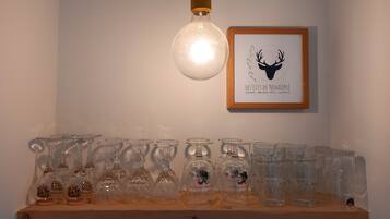 A shelf with various glassware, a framed picture of a deer head, and a hanging light bulb.