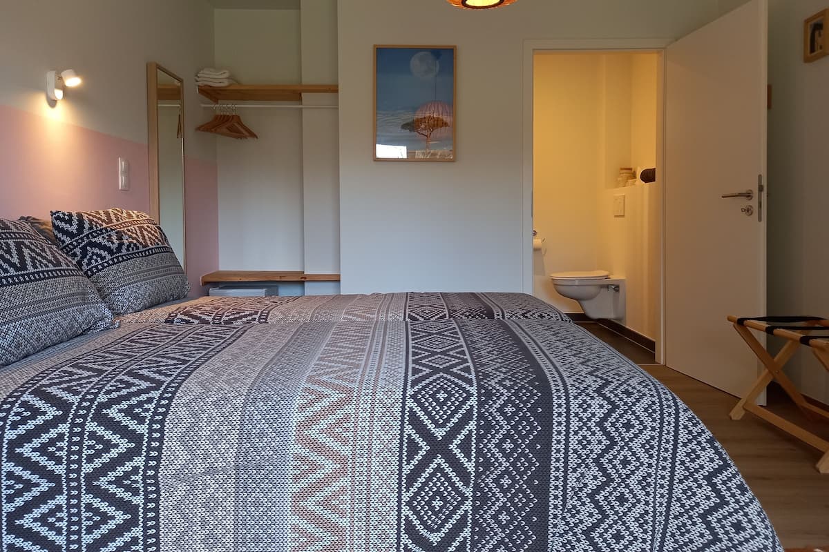 Un dormitorio con una cama grande, un banco de madera, una lámpara colgante y un cuadro en la pared.