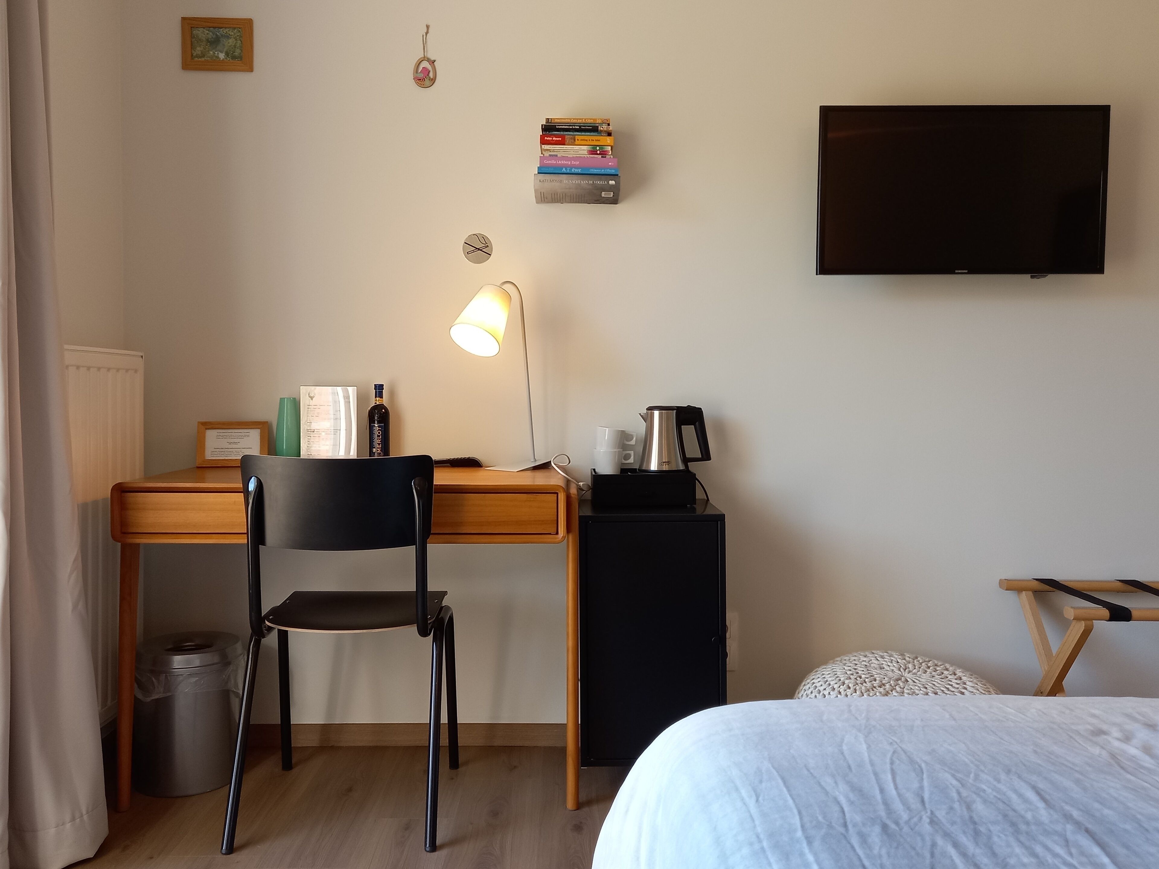 Een hotelkamer met een houten bureau, een zwarte stoel, een televisie, een boekenplank, een lamp, een koffiezetapparaat en een bed.